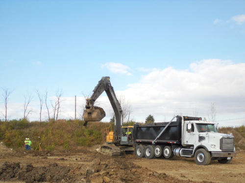 Excavator loading contaminated soil into a dump truck during a remediation dig