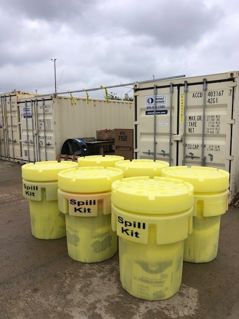 Six yellow 95 gallon spill kits staged in front of storage containers